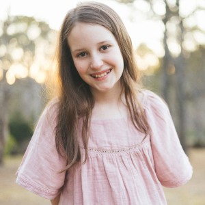 Elke smiling outside in a pink dress with trees in the background