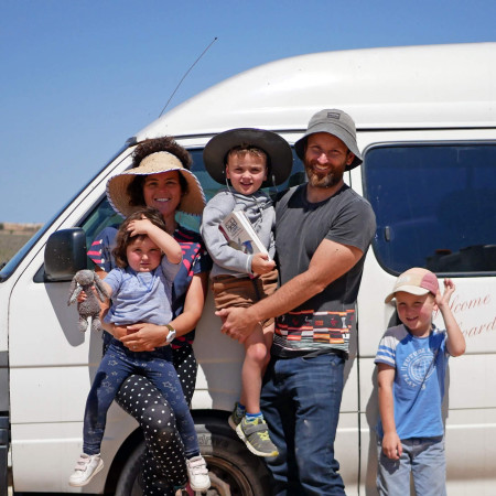 Joe and Katherine holding their kids and standing in front of their white van in outback Australia.